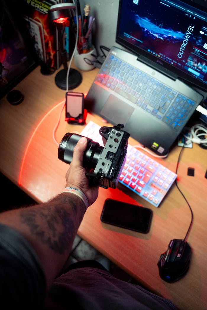 A photographer sets up on a tech-savvy desk with a DSLR, laptop, and colorful lighting.